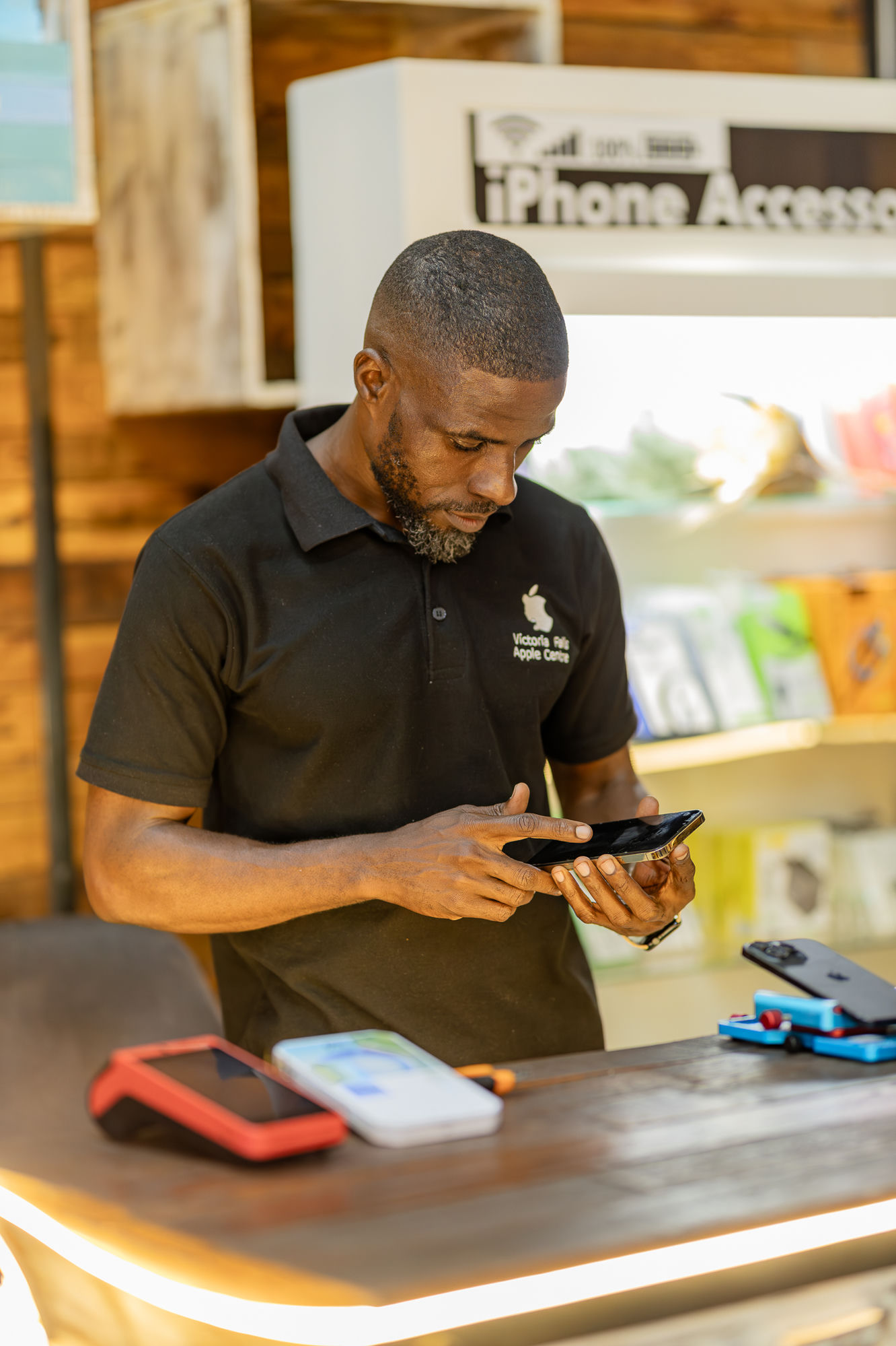 A Victoria Falls Apple Centre technician inspecting an iPhone at the counter